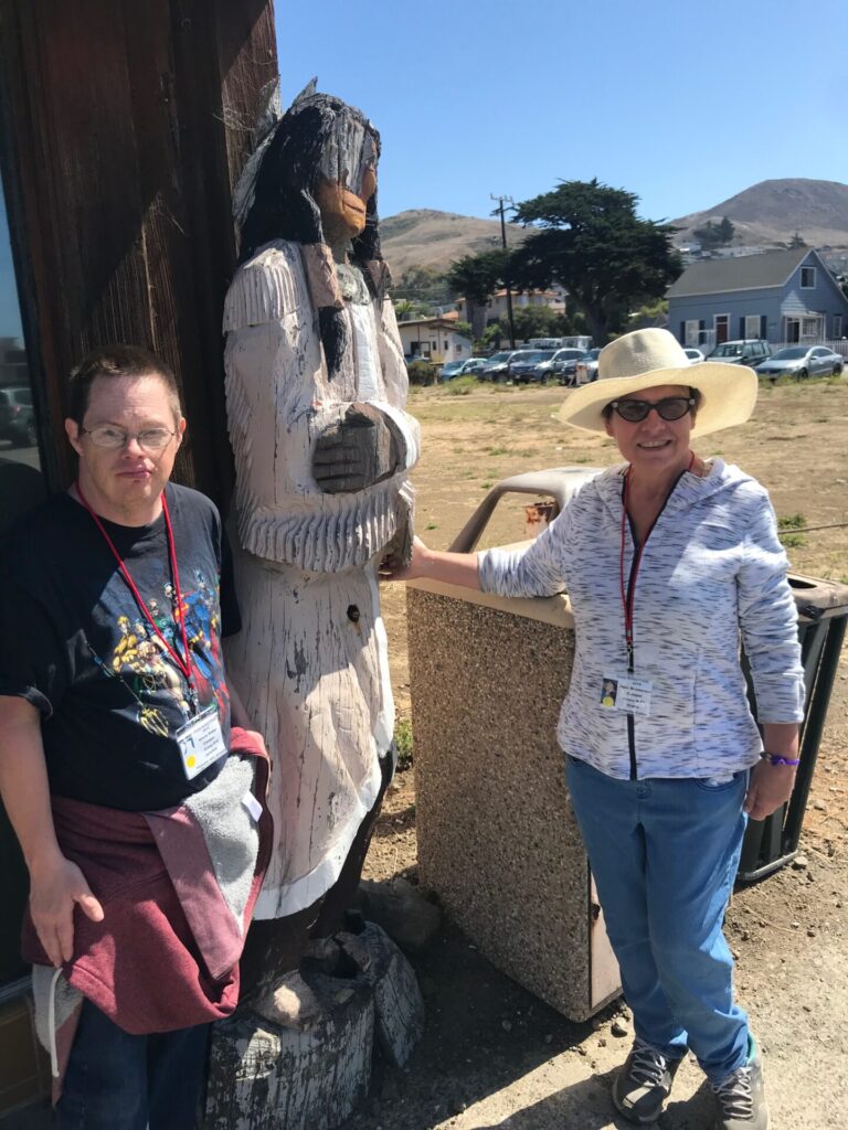 Two UCP members posing next to a wooden statue at Camp Kelley Creek