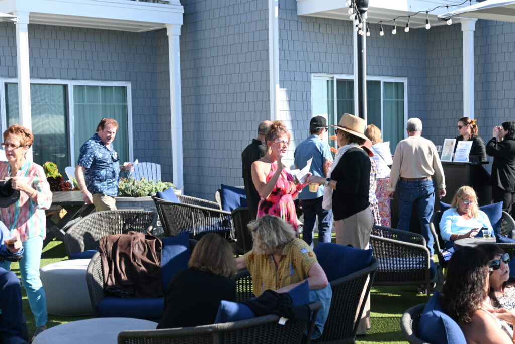 Participants and patrons enjoying the 2024 Celebration by the Sea event. Various people interacting, some sitting at tables, and some standing and conversing.
